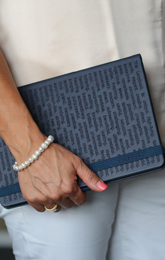 Hand hält ein Notizbuch mit typografischer Oberflächenprägung und farblich abgestimmtem Gummiband im Business-Alltag