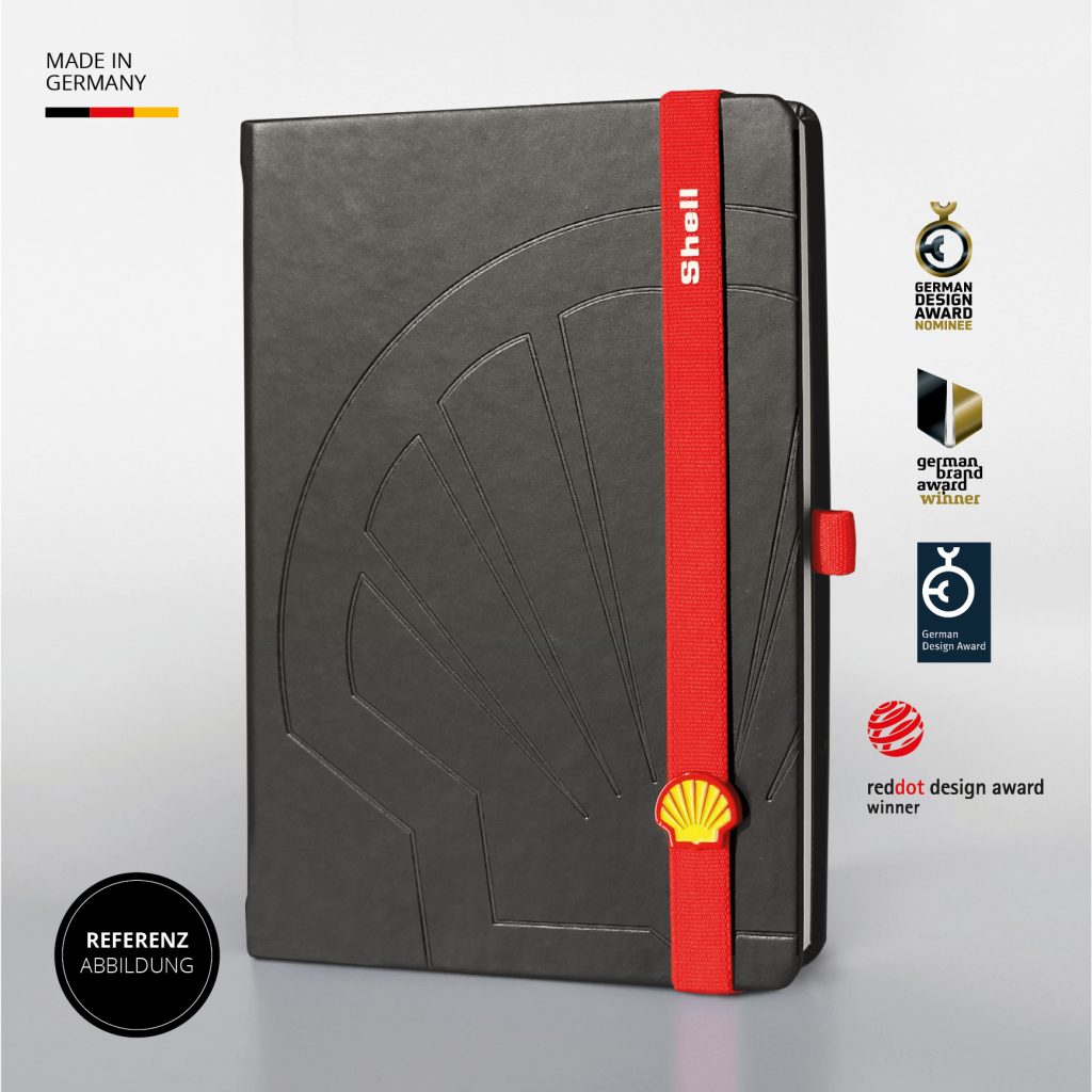Schwarzes Notizbuch mit großflächiger Shell Blindprägung, rotem Lanyband mit Shell Logo Button, Referenzabbildung mit Designauszeichnungen