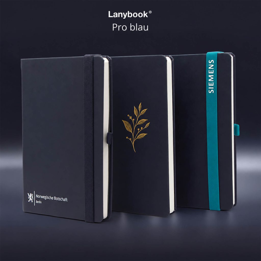 Drei dunkelblaue Lanybook Pro Notizbücher mit elastischem Verschlussband und individuellen Veredelungen. Die Bücher zeigen unterschiedliche Logo- und Prägevarianten, darunter eine goldene Prägung sowie ein türkisfarbenes Verschlussband mit weißem SIEMENS-Logo.