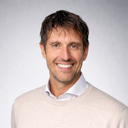 Porträt eines Mannes mit dunklem Haar und hellem Pullover vor neutralem grauem Studiohintergrund, Mitarbeiterfoto eines Notizbuchherstellers