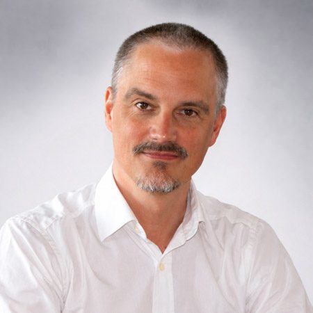 Porträt eines Geschäftsmanns im weißen Hemd vor neutralem Hintergrund mit direktem Blick in die Kamera.